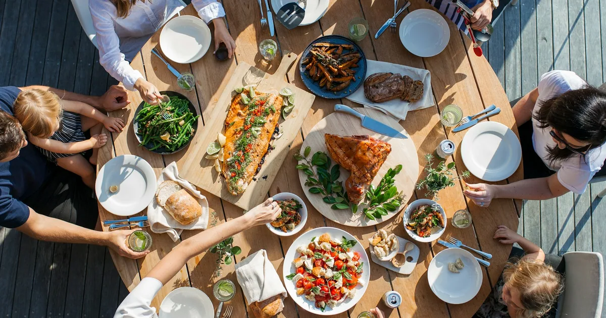 Familie samlet rundt et langbord med fisk, kylling, salater og grønnsaker — mat som er naturlig glutenfri